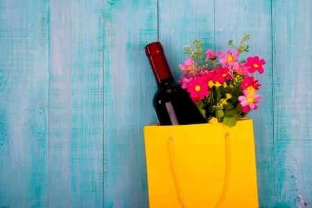 Thank your teachers with puns. Image of a bottle of wine and flowers in a gift bag.